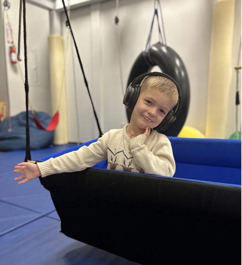 A child smiling in a therapy swing at the Oakland center